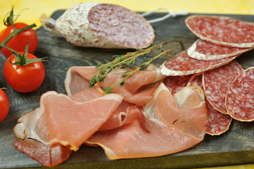 Slices of salami and Parma ham on a wooden board. In the frame, a few cherry tomatoes. Close-up. Macro photography.