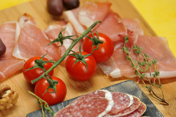 Slices of salami and Parma ham on a wooden board. In the frame, a few cherry tomatoes, a branch of thyme. Close-up. Macro photography.