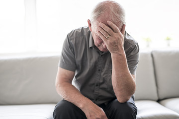 senior man thinking and sitting on sofa at home like sad