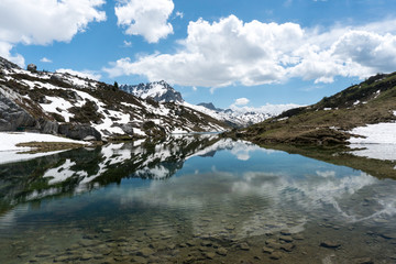 gorgeous mountain lake in the Alps with reflections and snow remnants