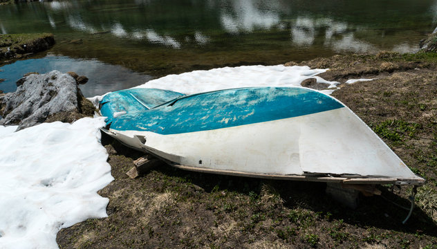 idyllic pristine mountain lake with a broken boat on the shore and snow fields
