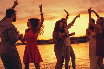 Group of young people have a party by the river during the sunset