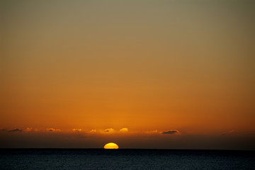 orange sunset as sun settles into sea below low clouds above