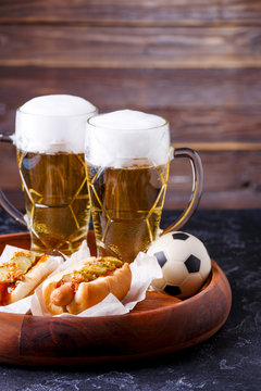 Image of two mugs of beer and hot dogs on wooden tray with football