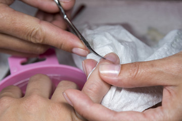 Obraz na płótnie Canvas Closeup of manicure applying, cutting the cuticle with scissors. Woman in nail salon receiving manicure by professional beautician. Manicure process in beauty salon, close up