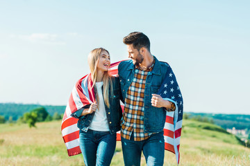 stylish couple with american flag on rural meadow, independence day concept