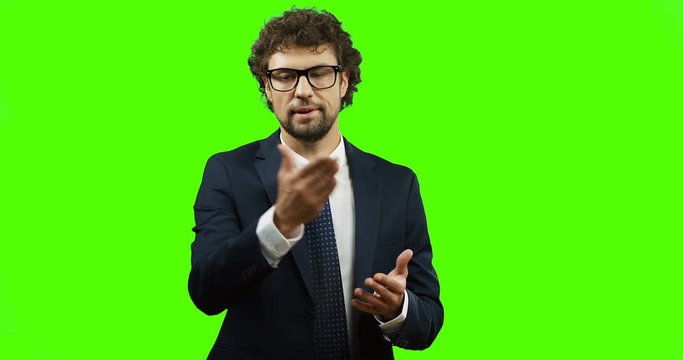 Good looking Caucasian businessman in glasses, suit and tie standing on the chroma key background and explaining something with gestures. Green screen.