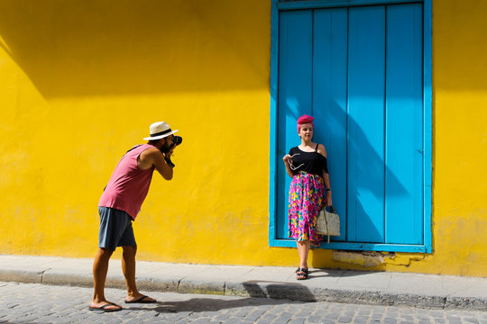 Man taking a photo of a girl against a yellow wall