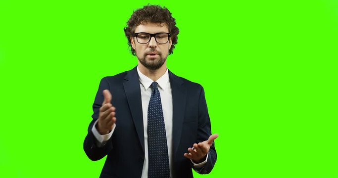 Caucasian handsome man in glasses, suit and tie standing on the chroma key background, talking and explaining something with hands gestures. Green screen.