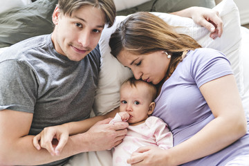 Portrait of beautiful young parents and cute baby on bed