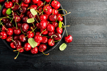 Fresh cherry on black plate on black wooden background. Top view, copy space