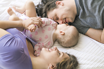 Portrait of beautiful young parents and cute baby on bed