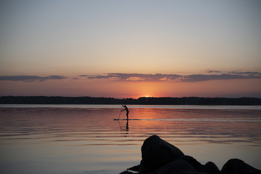 Surfer paddelt auf einem Surfbrett bei Sonnenuntergang