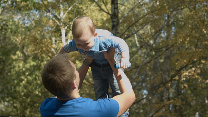 Dad tosses son into the air in an autumn Park. Happy family.