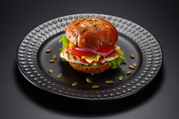 The burger with meat is served on a black plate. Decorated with different seeds.