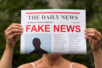 Woman holding up a newspaper with the headline fake news