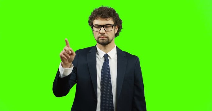Caucasian man in the suit standing on the green screen background, scrolling and taping in the air on the Chroma key.