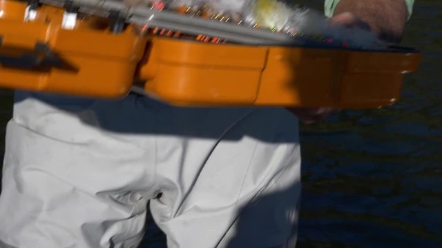 Fly fisherman selects a fly from a colorful box full of fishing flies