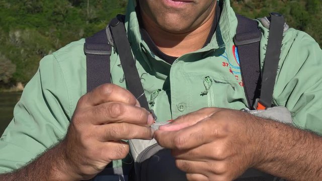 Fisherman skillfully ties a fishing knot in his line joining two sections of line in slow motion