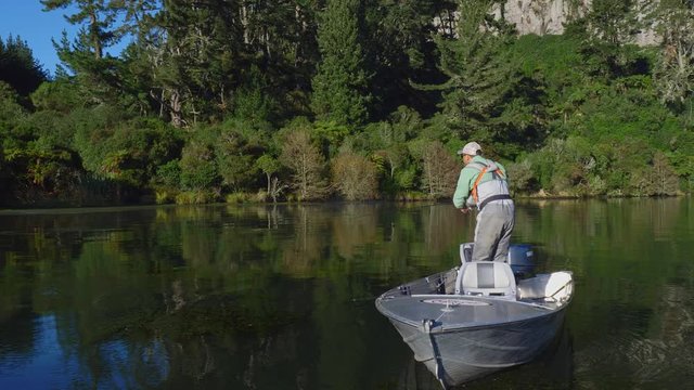 Fly fisherman casting his line from a boat in Lake Whakamaru in New Zealand