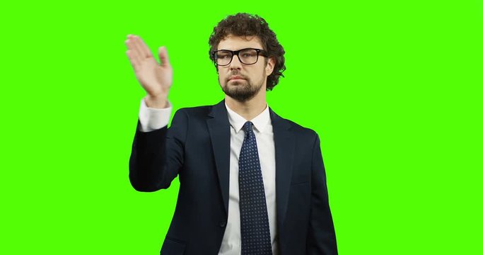Good looking man in the glasses, suit and tie standing on the chroma key background, scrolling and taping in the air. Green screen.