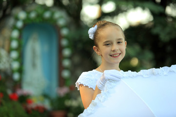 Śliczna mała dziewczynka w białej sukience na tle kapliczce.