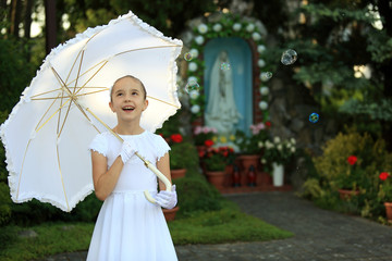 Śliczna mała dziewczynka w białej sukience na tle kapliczce.