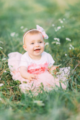 Portrait of happy joyful child in white dress over green grass background. Happy little baby girl in the park. Family concept