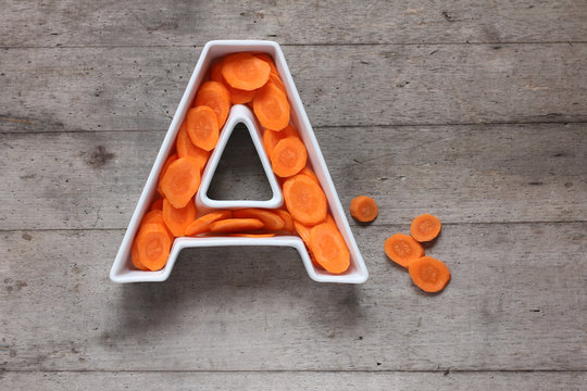 Vitamin A in food concept. Plate in the shape of the letter A with sliced fresh carrots on wooden background. Flat lay.