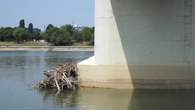 Broken tree stuck on the concrete pillar of the river bridge creating cascades