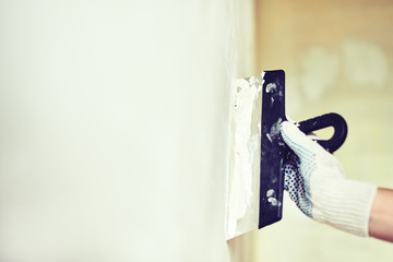Spatula with putty in hand. Worker puts of plaster on wall.