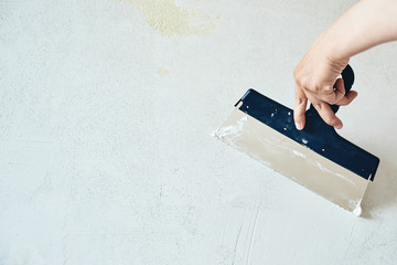 Spatula with putty in hand. Worker puts of plaster on wall.