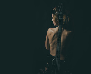 Girl with nude back stand with guitar neck as spine, black background. Lady guitarist with sexy appearance naked. Rock star concept. Girl nude and sexy enjoy rock and roll lifestyle, rear view