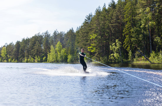 Young pretty slim brunette woman in wetsuit riding wakeboard on