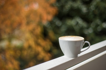 Close up white coffee cup with heart shape latte on balcony railing