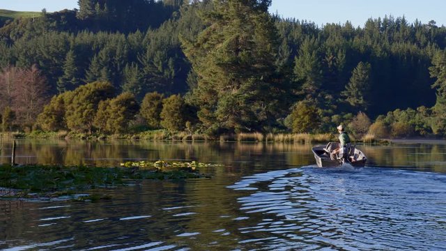 Fly fisherman in boat driving on scenic Lake Whakamaru in New Zealand to go fishing