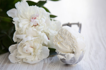Obraz na płótnie Canvas Ice cream in ice cream scoop with white peony blossom flowers over white wooden background, close-up.
