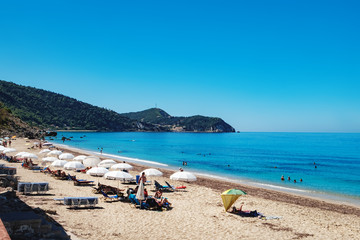 Fototapeta na wymiar View of the Pefkoulia Beach, Lefkada island, Greece. Tourists, sunbeds and umbrellas on idyllic sunny day.