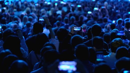 Audience listens to the lecturer at the conference hall taking video on smartphones