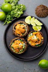 Fresh opened sea urchins. Caviar of sea urchins with onion, cilantro and lemon inside of shell of sea urchins. Top view, Black plate, gray slate background
