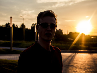 Fototapeta premium handsone young man in sunglasses and polo looking forward walkng in the city during golden hour