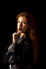 Redhead latin girl with black jacket on black background making the silence symbol