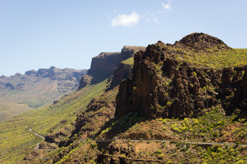 Naklejka premium Windy road alongside slope of Degollada de las Yeguas canyon in Gran Canaria. Green and brown valley unique landscape. Sightseeing tour, summer travel destination concept