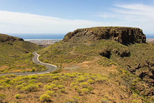 Windy road by Degollada de las Yeguas canyon in Gran Canaria with sea views on the background. Green and brown valley unique landscape. Sightseeing tour, summer travel destination concept