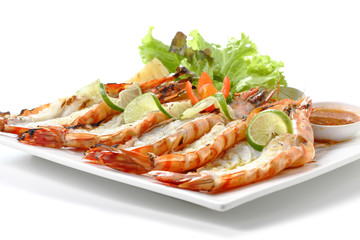 Roasted sliced tiger shrimps with baked potato, slice of lemons, vegetables & chili sauce on square plate, isolated on white background, Closeup macro low angle front side view. focus middle of food.