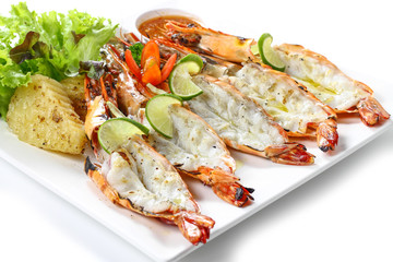 Grilled cut-off black tiger prawns with baked potato, slice of limes, fresh vegetables & chili sauce on square plate, isolated on white background, Close-up macro high angle view, Focus middle of food