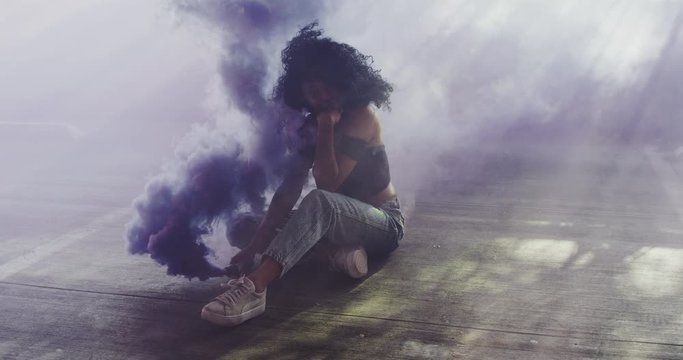Beautiful young woman modeling with purple smoke grenade in dramatic moody lighting 