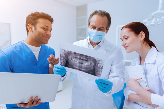 Perfect example. Positive delighted foreign student turning head to the mentor while holding laptop in right hand and keeping smile on his face
