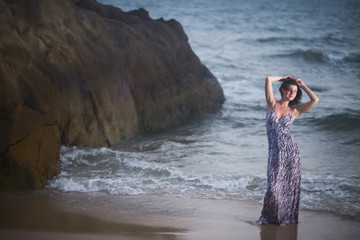 Young beautiful woman posing in sea water on sea and rock background