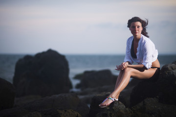 Fototapeta na wymiar Young beautiful woman sitting on stones in the evening against the sea